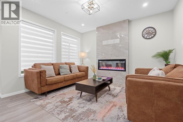 Living room featuring two brown leather sofas, a dark wood coffee table, and a contemporary fireplace with a marble surround. - 39 Herron Rise Ne, Calgary