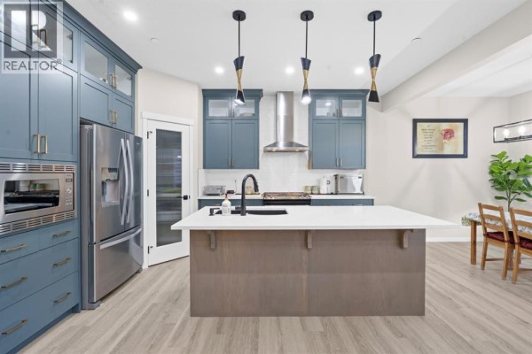 Kitchen with blue cabinets, stainless steel appliances, a white island with a sink, and light wood-look flooring. - 39 Herron Rise Ne, Calgary