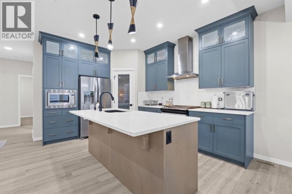 Spacious kitchen with blue upper cabinets, grey lower cabinets, a central island, stainless steel appliances, and pendant lighting. - 39 Herron Rise Ne, Calgary