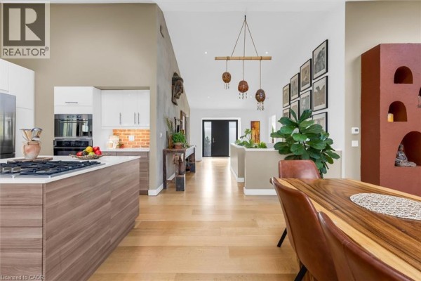 Open-concept kitchen with modern appliances, wooden dining table, and decorative wall art. - 39 Hilts Drive, Stoney Creek