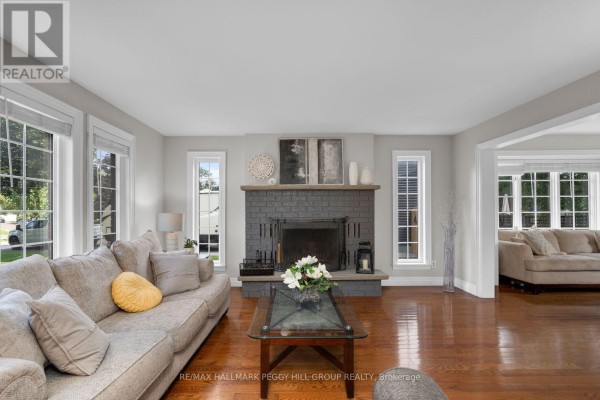 Living room with a large grey sectional sofa, a glass coffee table, and a dark grey brick fireplace. - 39 Howard Drive, Oro Medonte