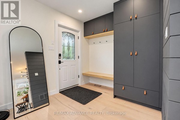 Entranceway with light wood floors, dark grey built-in storage, and a tall arched mirror. - 39 Janet Boulevard, Toronto