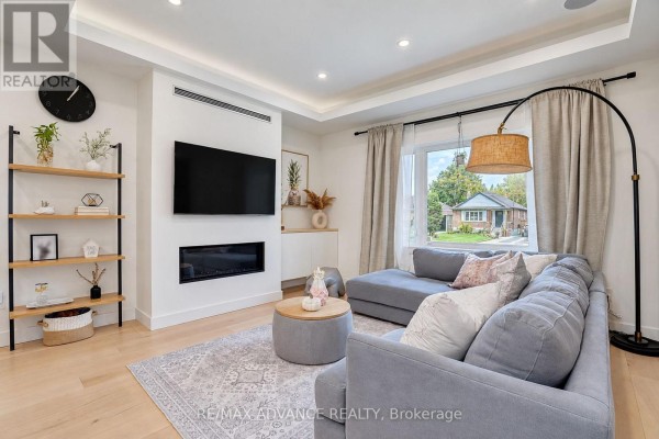 Living room with grey sectional sofa, ottoman coffee table, built-in fireplace, and window view. - 39 Janet Boulevard, Toronto