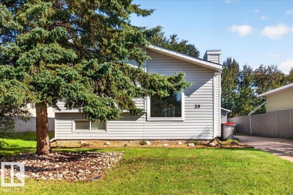 A large evergreen tree is in front of the light grey sided house at 39 Mcnabb Cr. - 39 Mcnabb Cr, Stony Plain