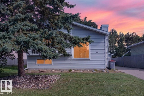 The light grey house with a large window at 39 Mcnabb Cr is viewed at dusk. - 39 Mcnabb Cr, Stony Plain