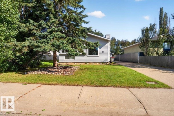 View of the light grey house at 39 Mcnabb Cr from the sidewalk with a driveway. - 39 Mcnabb Cr, Stony Plain