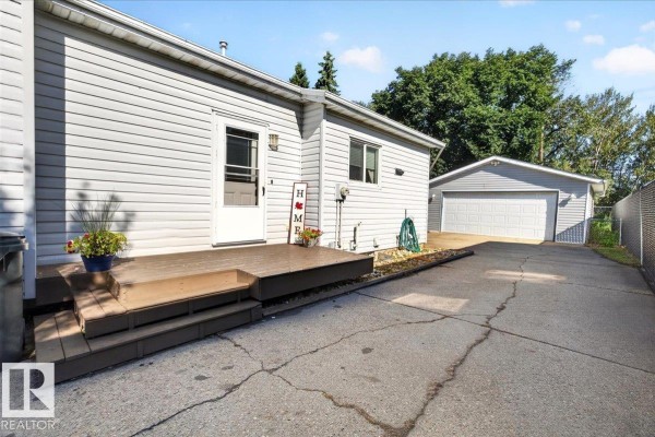 Rear exterior of the house showing a wooden deck, back door, and detached garage. - 39 Mcnabb Cr, Stony Plain