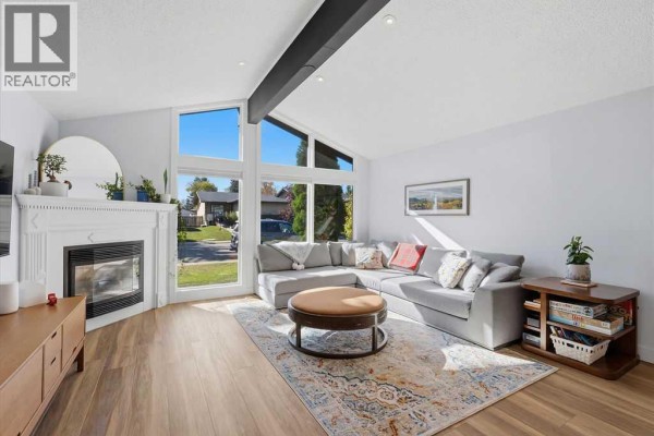 Living room with a grey sectional sofa, a circular coffee table, a fireplace, and large windows. - 39 Midridge Close Se, Calgary