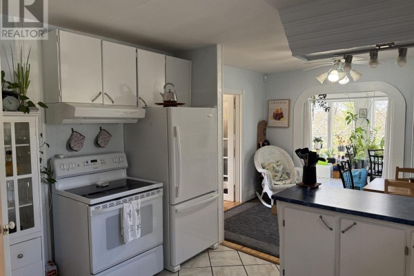 Kitchen with a white stove and refrigerator, adjacent to a sunroom with a wicker chair. - 39 Munroe Ave Extension, Westville Road