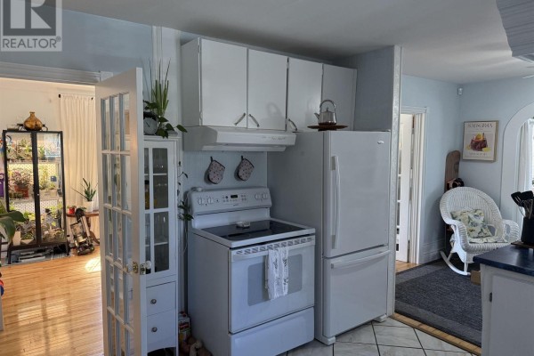 Kitchen area with white cabinets and appliances, opening into a sunroom with a rocking chair. - 39 Munroe Ave Extension, Westville Road