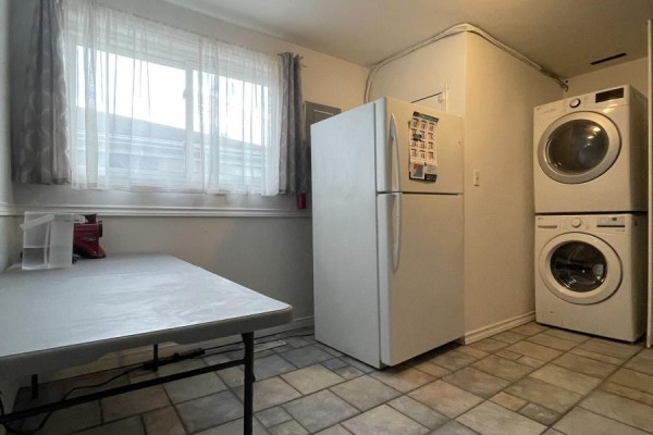 Room with folding table, large window with grey curtains, white refrigerator, and stacked washer and dryer. - 39 Richardson Drive S, Aurora