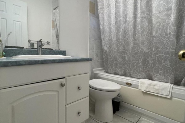 Bathroom with white vanity, sink, toilet, bathtub with grey floral shower curtain, and tiled floor. - 39 Richardson Drive S, Aurora