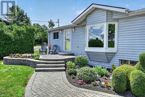 Close-up of the entrance to a light blue bungalow with a bay window and landscaped gardens. - 39 Riverside Drive, Kawartha Lakes