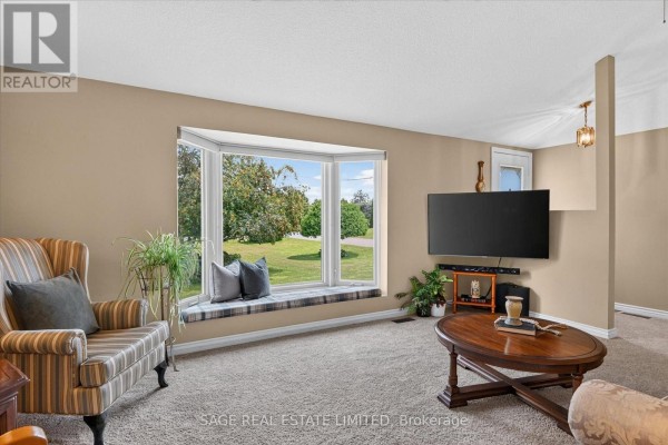 Living room with a large bay window, striped armchair, coffee table, and television. - 39 Riverside Drive, Kawartha Lakes