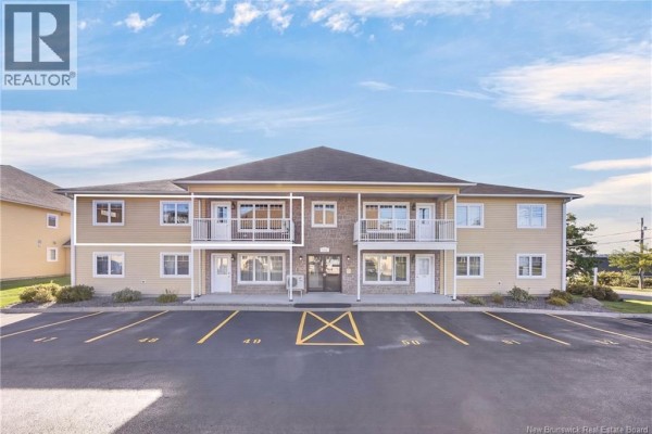 Front view of the apartment building with designated parking spaces and manicured landscaping under a blue sky. - 39 Sunny Brae Drive Unit# 214, Fredericton