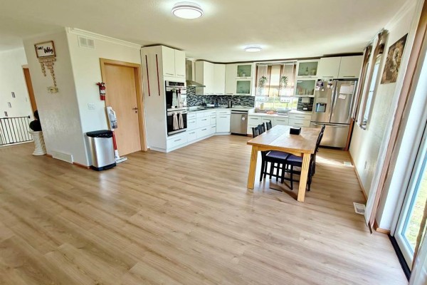 Open-concept kitchen and dining area with white cabinets, stainless steel appliances, and a wooden dining table. - 39044 Road 34n Road, La Broquerie