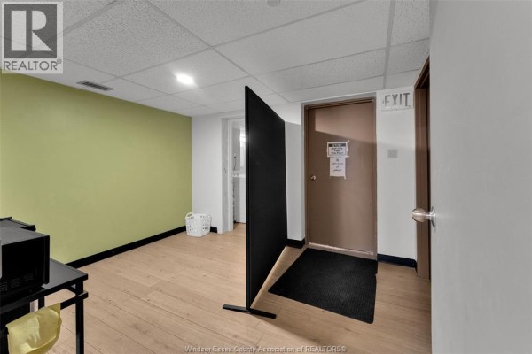 Small room with green accent wall, wood floor, and exit door. - 3905-3911 Tecumseh Road East, Windsor