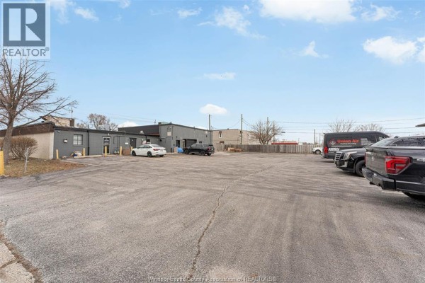 Rear exterior of commercial buildings with asphalt parking and vehicles. - 3905-3911 Tecumseh Road East, Windsor