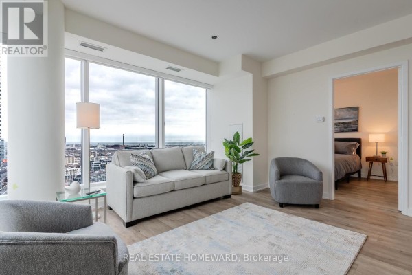 Living room with sofa, chairs, large windows, and view of city. - 3907 - 28 Freeland St. Street, Toronto