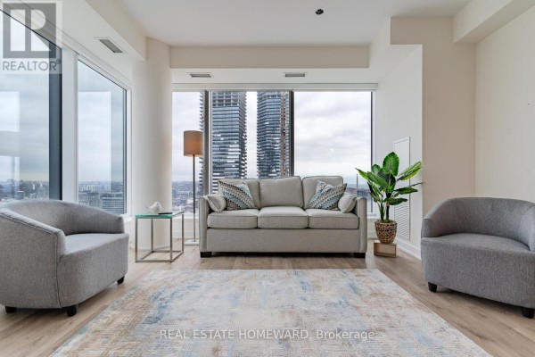 Living room with sofa, chairs, large windows, and city view. - 3907 - 28 Freeland St. Street, Toronto