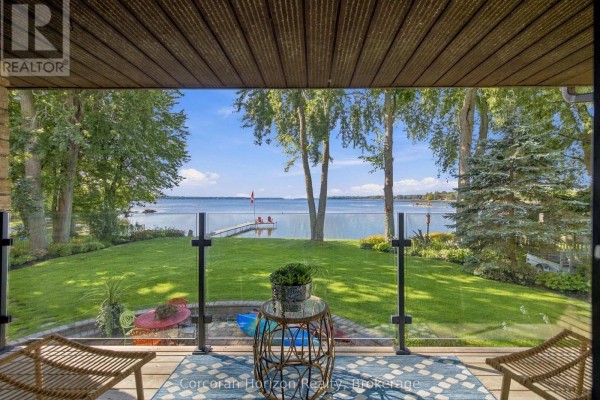 View from a covered deck overlooking a grassy yard, lake, and distant treeline. - 3909 Treeline Drive, Severn
