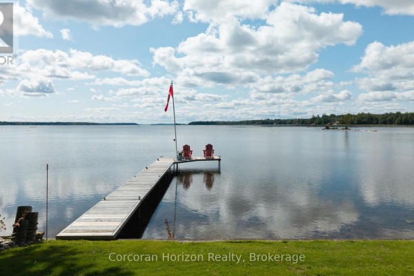 Wooden dock with two red Adirondack chairs on a calm lake under a blue sky. - 3909 Treeline Drive, Severn
