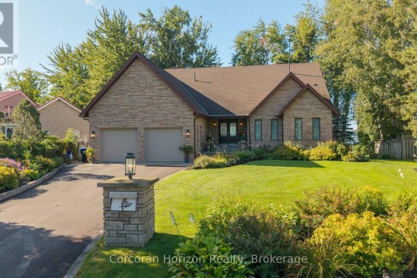 Front exterior of a stone home with a double garage, manicured lawn, and lush landscaping. - 3909 Treeline Drive, Severn