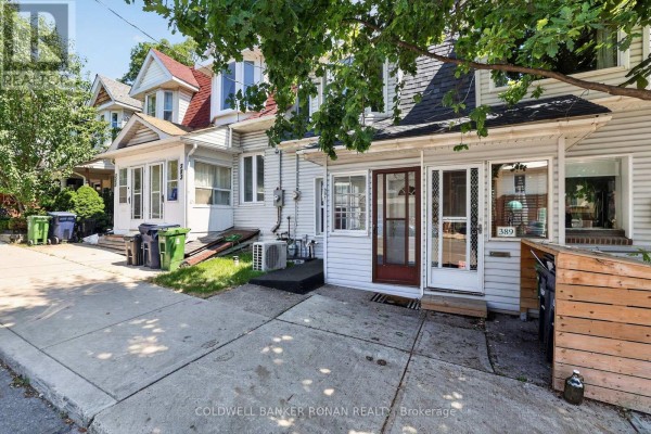 Side exterior view of white townhouse entrance with garbage bins. - 391 Jones Avenue, Toronto