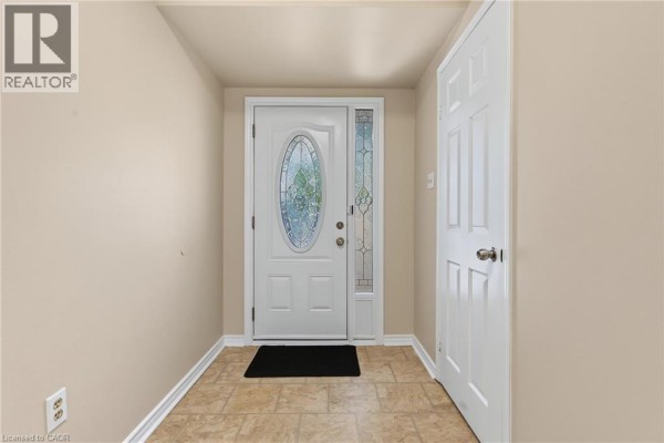 Interior foyer with beige walls, tiled floor, and a white front door with glass accents. - 391 Stone Church Road E Unit# 14, Hamilton