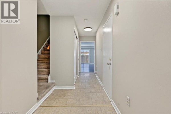 Hallway inside a townhouse with beige walls, tiled floor, and stairs leading to the second level. - 391 Stone Church Road E Unit# 14, Hamilton