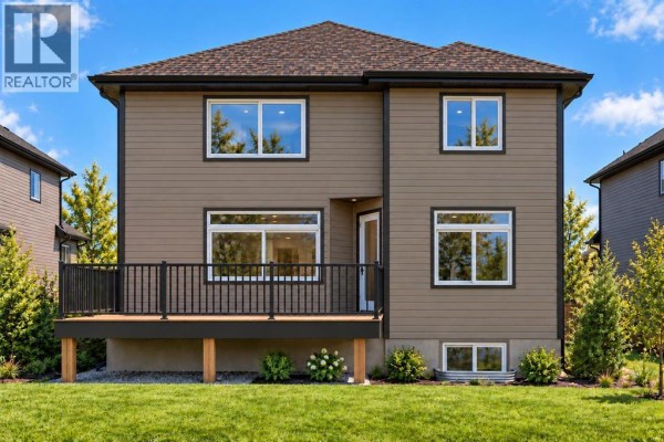 Rear exterior of the house showing a wooden deck and backyard lawn. - 391 Waterford Grove, Chestermere