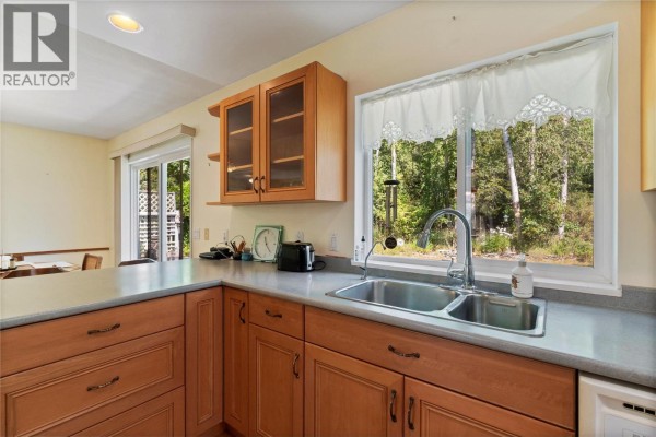 Kitchen sink area with double basin sink, wooden cabinets, and a large window overlooking greenery. - 3915 Express Point Road, Scotch Creek
