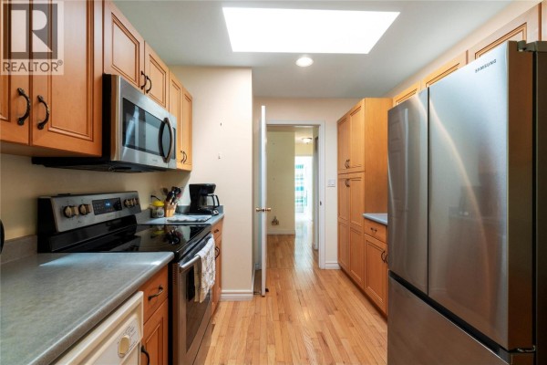View down the kitchen toward a hallway and another room, featuring stainless steel refrigerator and wood floor. - 3915 Express Point Road, Scotch Creek