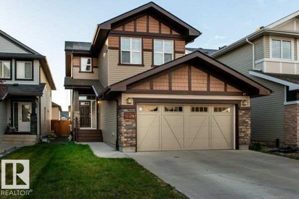 Front exterior of a two-story house with beige siding, brown trim, and a double garage door. - 3917 171a Av Nw, Edmonton