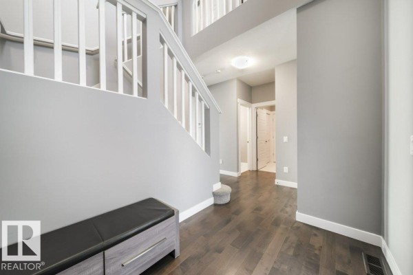 Interior foyer with grey walls, dark wood floors, a staircase, and a bench. - 3917 171a Av Nw, Edmonton