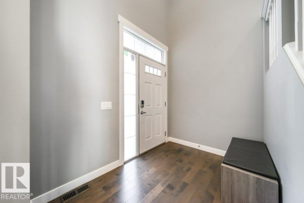 Interior foyer with grey walls, dark wood floors, a white front door with sidelights, and a bench. - 3917 171a Av Nw, Edmonton