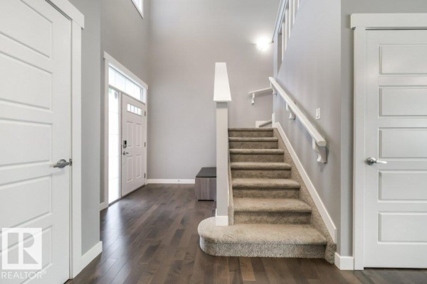 Interior foyer with grey walls, dark wood floors, a carpeted staircase, and white doors. - 3917 171a Av Nw, Edmonton