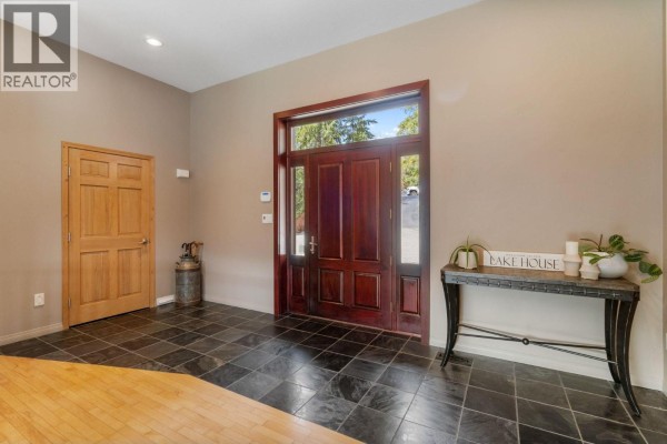 Open-concept living space with wood floors, a dark wood buffet, fireplace, and large windows with lake views. - 3918 Parri Road, Sorrento