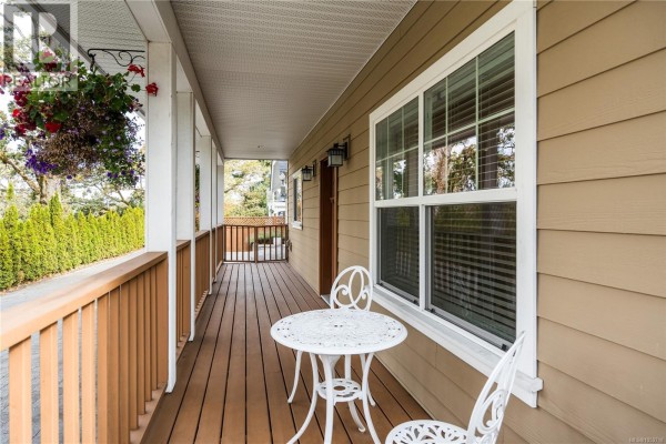 Covered porch with a white table and chairs next to a large window. - 3919 Blenkinsop Rd, Saanich
