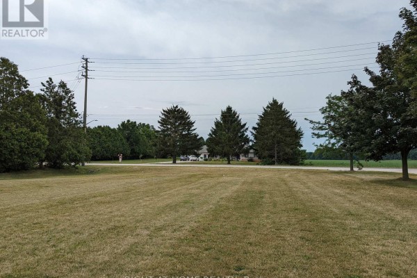 View across a dry grassy lawn towards a detached house with a circular driveway and utility pole. - 392 Second Street, Strathroy Caradoc