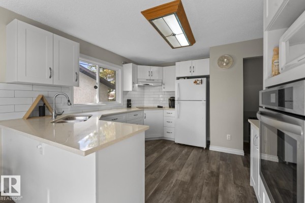 Kitchen showing white cabinets, a sink, microwave, oven, and refrigerator with wood laminate flooring. - 3920 52 Av, Cold Lake