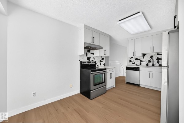 Compact kitchen with white cabinets, stainless steel appliances, and geometric tile backsplash. - 3924 26a Av Nw, Edmonton