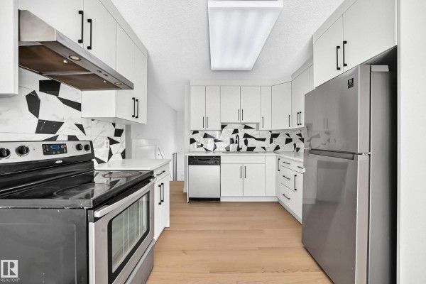 Kitchen showing white cabinetry, a stainless steel refrigerator, and light wood flooring. - 3924 26a Av Nw, Edmonton