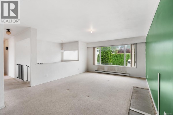 Living room with beige carpet, white walls, a green accent wall, and a large window. - 3931 Braefoot Pl, Saanich