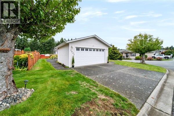 Side view of a beige mobile home with a white garage door and concrete driveway. - 3931 Excalibur St, Nanaimo