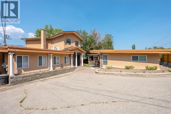 Exterior of the property showing tan stucco siding, stone accents, and pillars. - 3935 Lakeside Road, Penticton