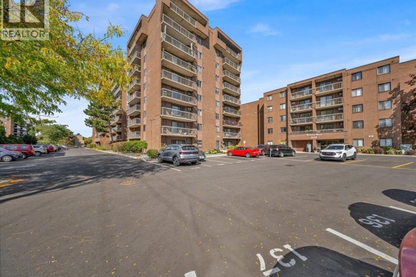 Exterior view of two connected brick apartment buildings with balconies and a parking lot. - 3936 Wyandotte Street East Unit# 206, Windsor
