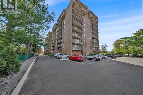 Exterior view of a brick apartment building with balconies and a paved parking lot. - 3936 Wyandotte Street East Unit# 206, Windsor