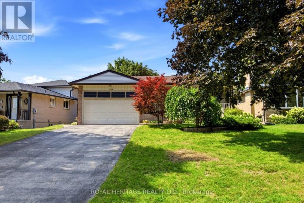 Wide shot of the residential property from the street, featuring a large driveway and front lawn. - 394 Amstel Court, Oshawa