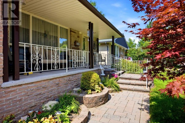 Close-up of the covered porch entrance with stone steps, brick accents, and decorative railing. - 394 Amstel Court, Oshawa